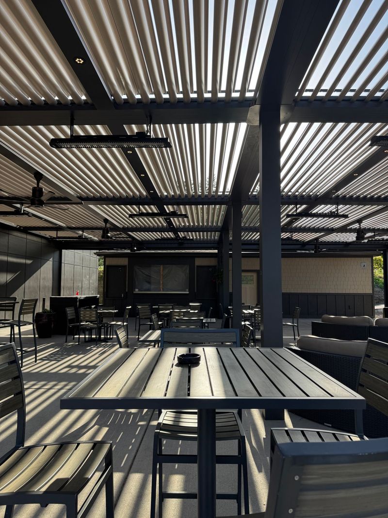 Aluminum pergola with louvers rotated fully open, sunlight streaming between the slats onto a patio dining area